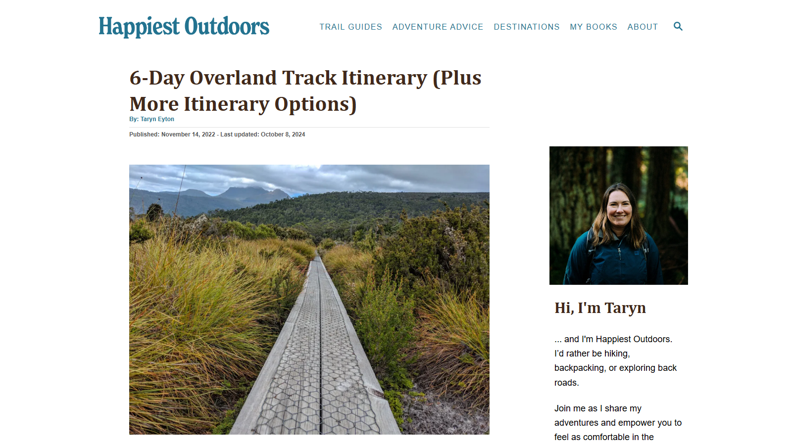 Article headed '6-Day Overland Track Itinerary (Plus More Itinerary Options)' with the byline 'By: Taryn Eyton' and a published date line, above a photograph of a raised metal-mesh boardwalk running straight through golden buttongrass moorland toward forested hills and a distant mountain range under grey cloud; a sidebar portrait sits beside 'Hi, I'm Taryn'