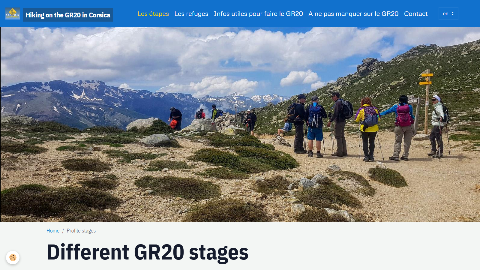A wide mountain photo of hikers with packs and poles pausing at a wooden signpost on a stony col, snow-streaked Corsican peaks and cloud behind, above the page heading 'Different GR20 stages'.