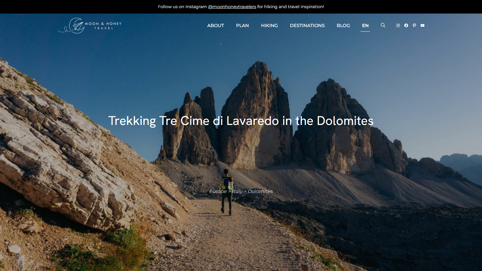 Full-screen photograph of a lone hiker walking a gravel path toward the three limestone towers of Tre Cime di Lavaredo under a deep blue sky, with the headline "Trekking Tre Cime di Lavaredo in the Dolomites" and the breadcrumb "Europe > Italy > Dolomites" centered over the image