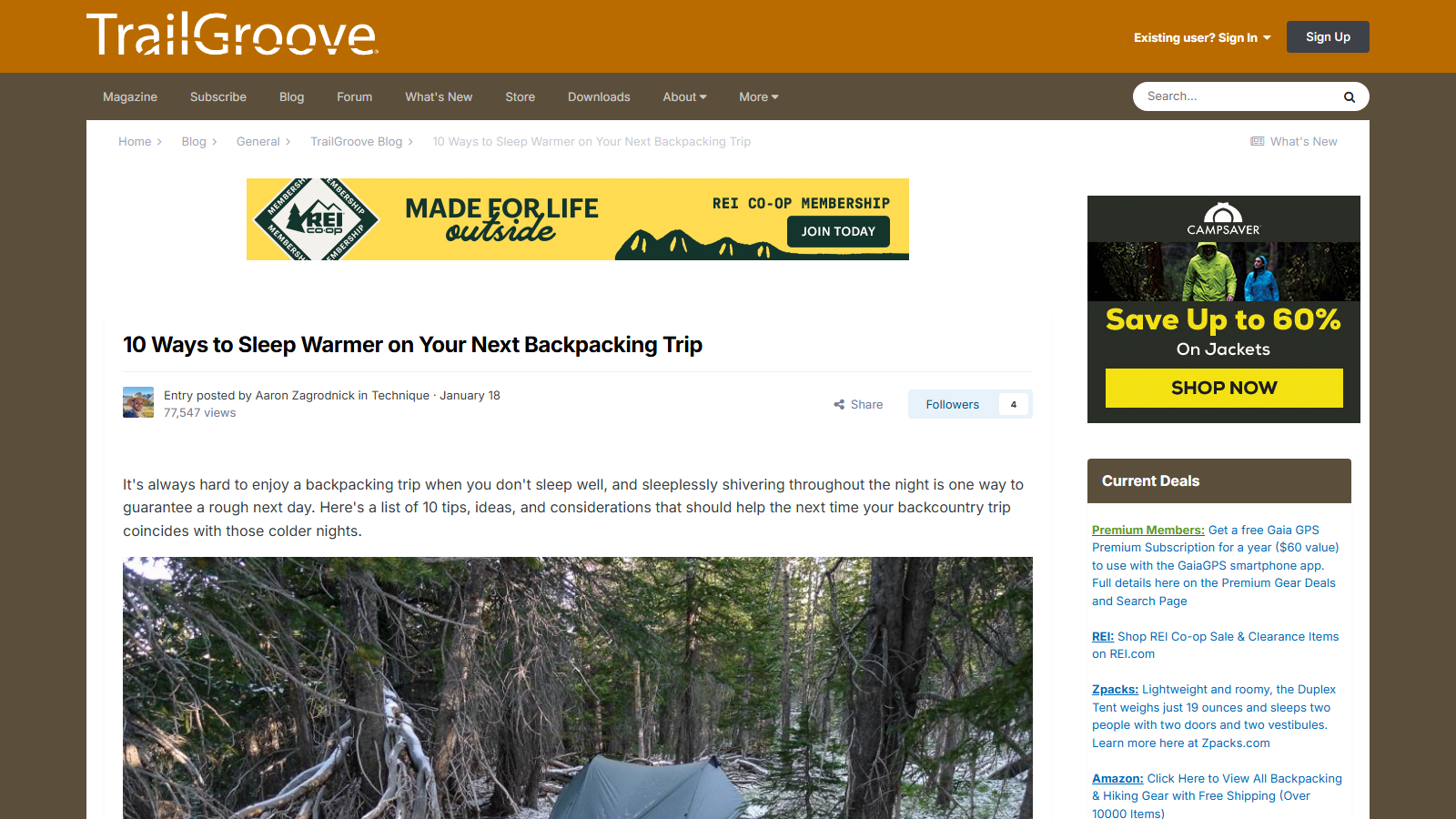TrailGroove blog entry headed '10 Ways to Sleep Warmer on Your Next Backpacking Trip', posted by Aaron Zagrodnick, with the intro paragraph above a photo of a green tent pitched among snow-dusted trees; an REI membership banner and a Current Deals sidebar surround the article
