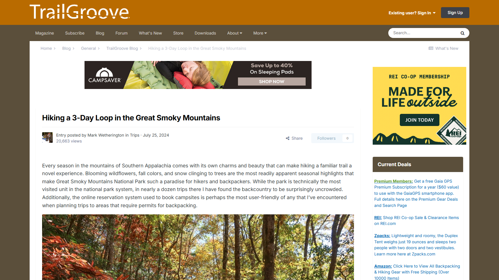 Orange TrailGroove masthead above a CampSaver sleeping-pad ad banner and the article "Hiking a 3-Day Loop in the Great Smoky Mountains" by Mark Wetherington, July 25 2024, showing its opening paragraph and a photo of an autumn forest of red and yellow leaves below; an REI Co-op membership ad and a "Current Deals" box of gear and subscription offers run down the right sidebar.
